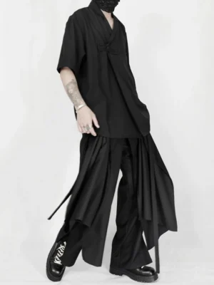 Side three-quarter view of black wide-leg draped trousers with hanging strap details and layered avant-garde panel