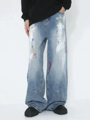 Front low-angle view of faded blue avant-garde paint splash wide-leg jeans with colorful graffiti brush strokes styled with a black top and chunky shoes