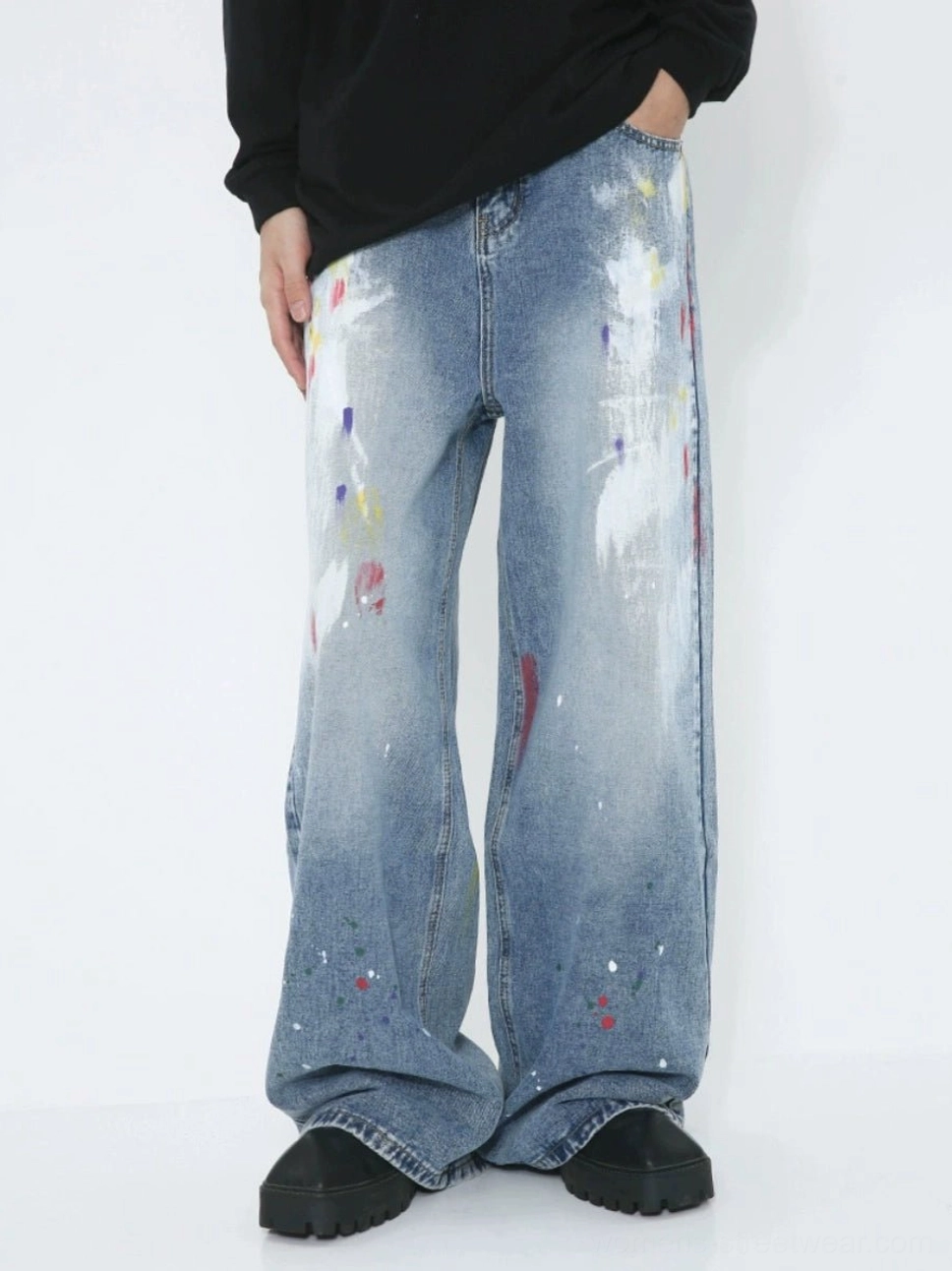 Front low-angle view of faded blue avant-garde paint splash wide-leg jeans with colorful graffiti brush strokes styled with a black top and chunky shoes