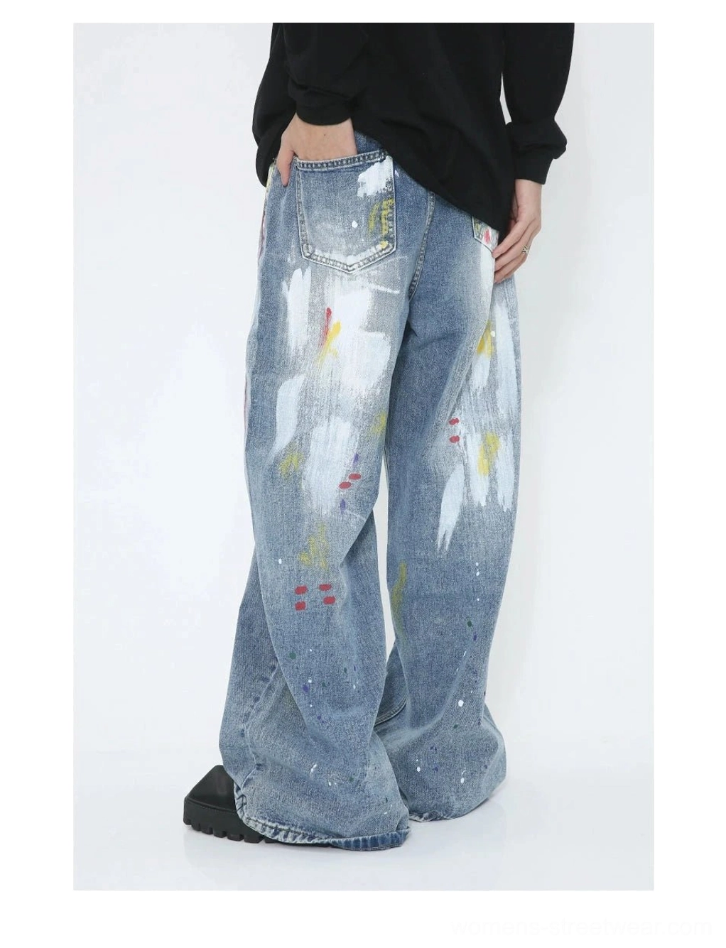 Rear three-quarter view of avant-garde wide-leg jeans with faded blue denim, colorful paint splashes and relaxed artistic streetwear silhouette
