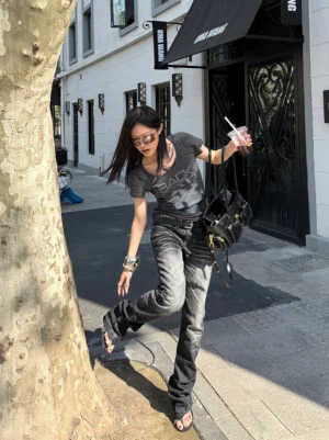 Female model wearing a charcoal gray BACK graphic scoop neck tee with faded vintage portrait print and dark jeans in an outdoor streetwear setting