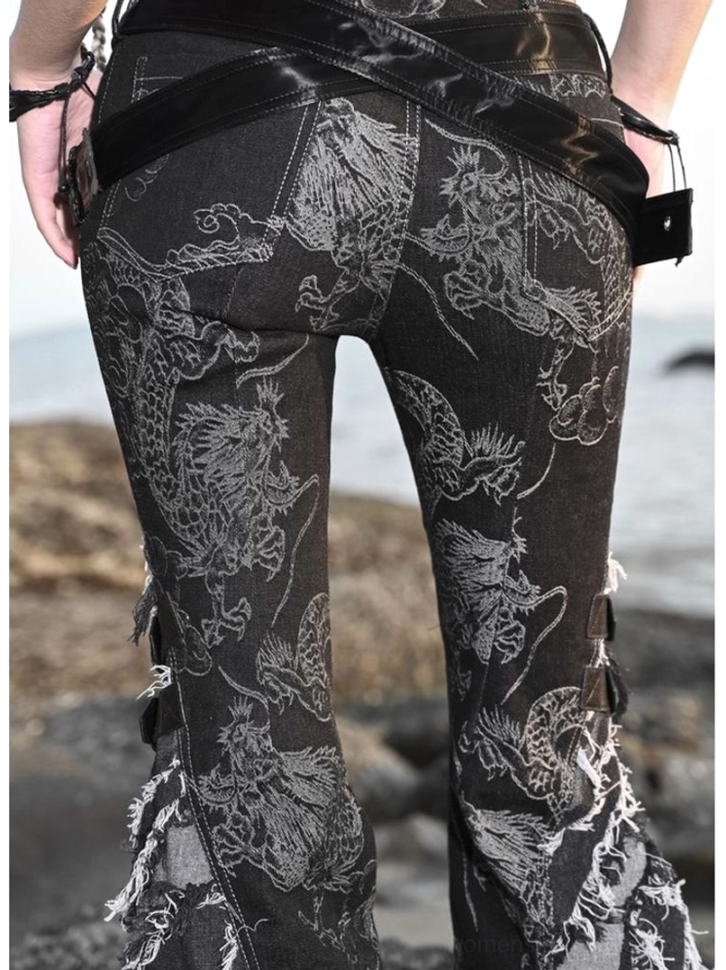 Back view of black dragon print flare jeans showing full grey dragon artwork, crossed leather waist belt, and distressed frayed bottom hems