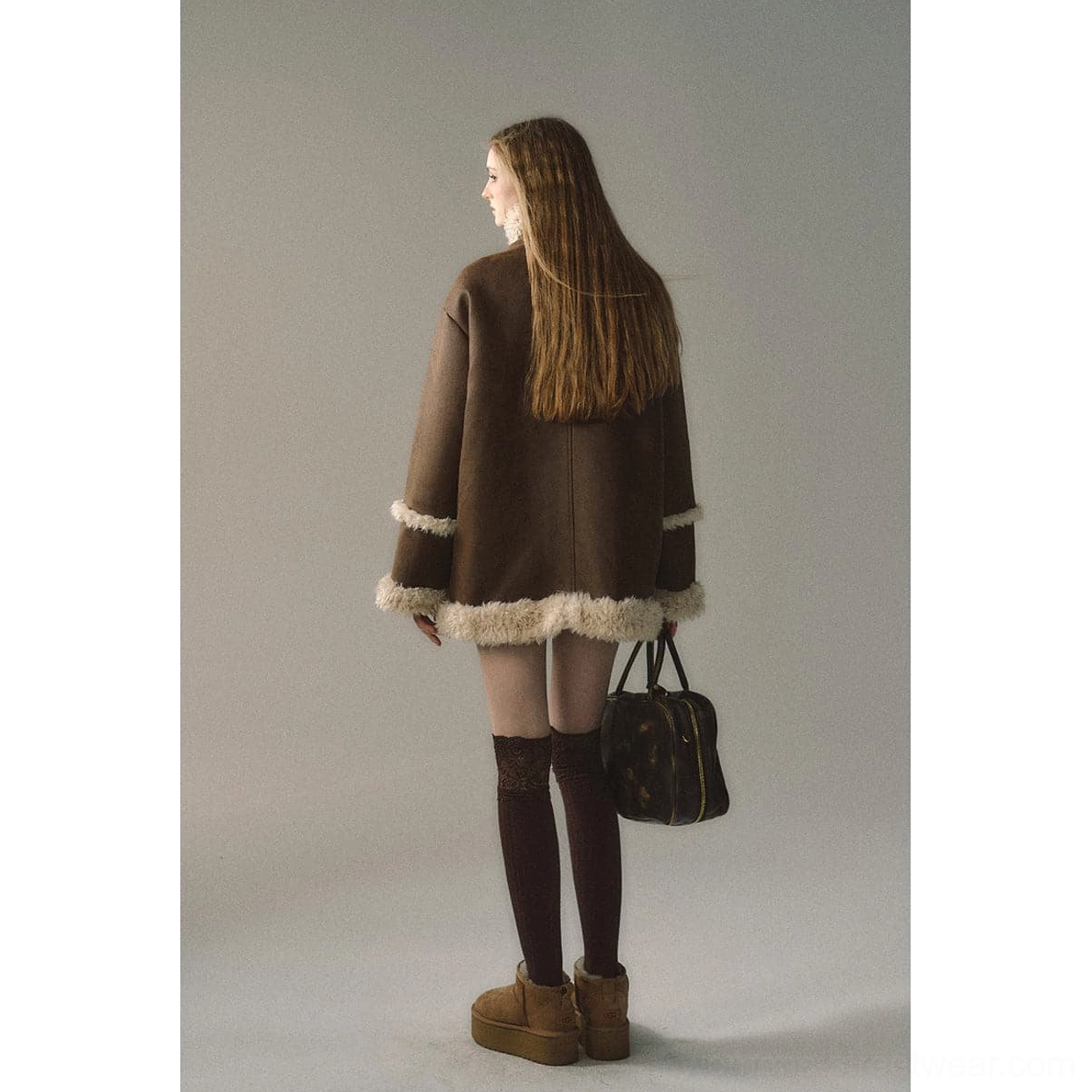 Back view of dark brown reversible suede shearling jacket with cream hem and cuffs styled with knee-high socks and brown platform boots
