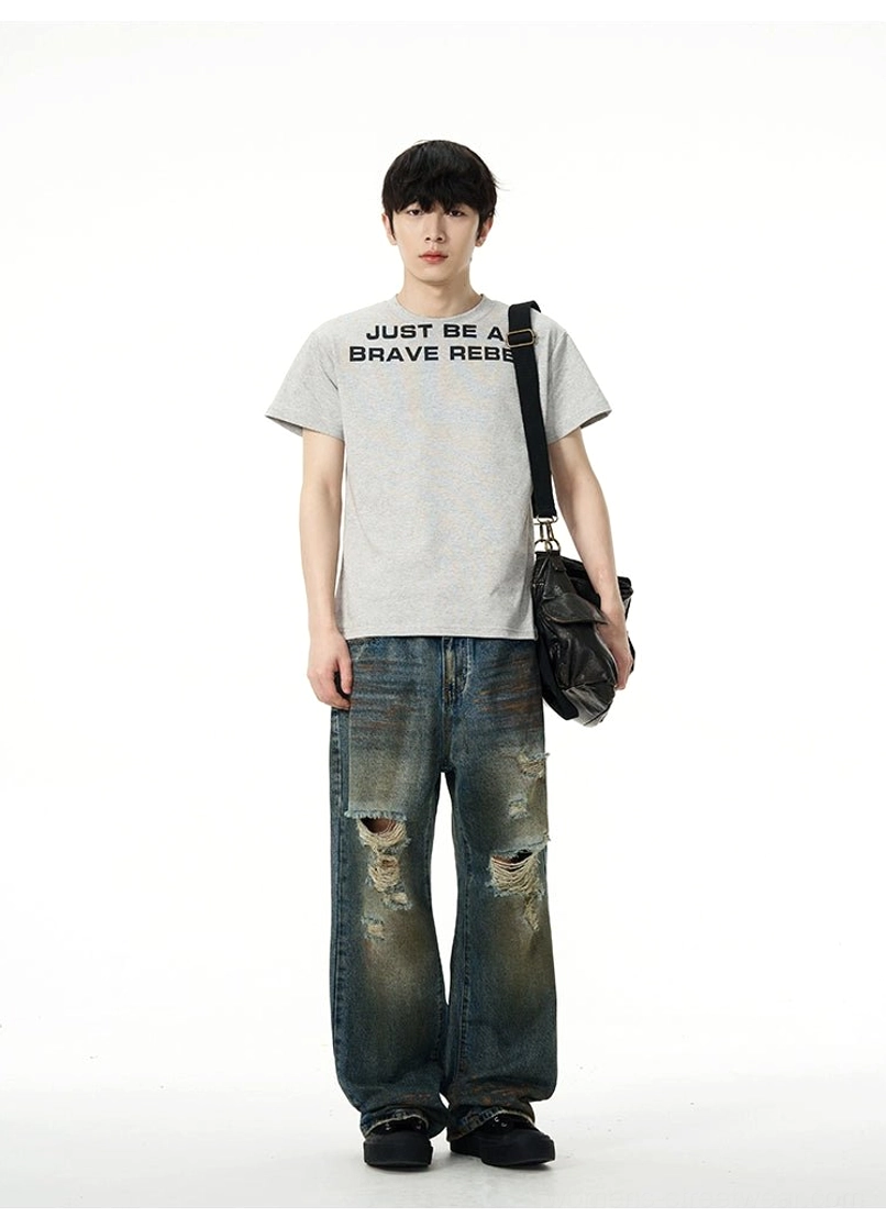 Male model wearing distressed baggy blue jeans with ripped details, five-pocket design, crossbody bag, and casual streetwear styling