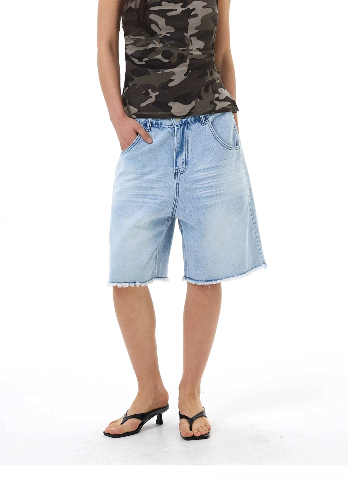 Side front view of baggy light blue denim Bermuda shorts with roomy pockets, relaxed straight legs, and frayed raw hems