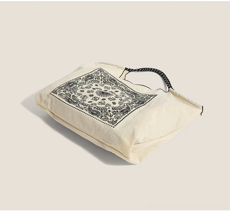 Flat lay of off white bandana paisley drawstring market tote bag with black dotted shoulder straps