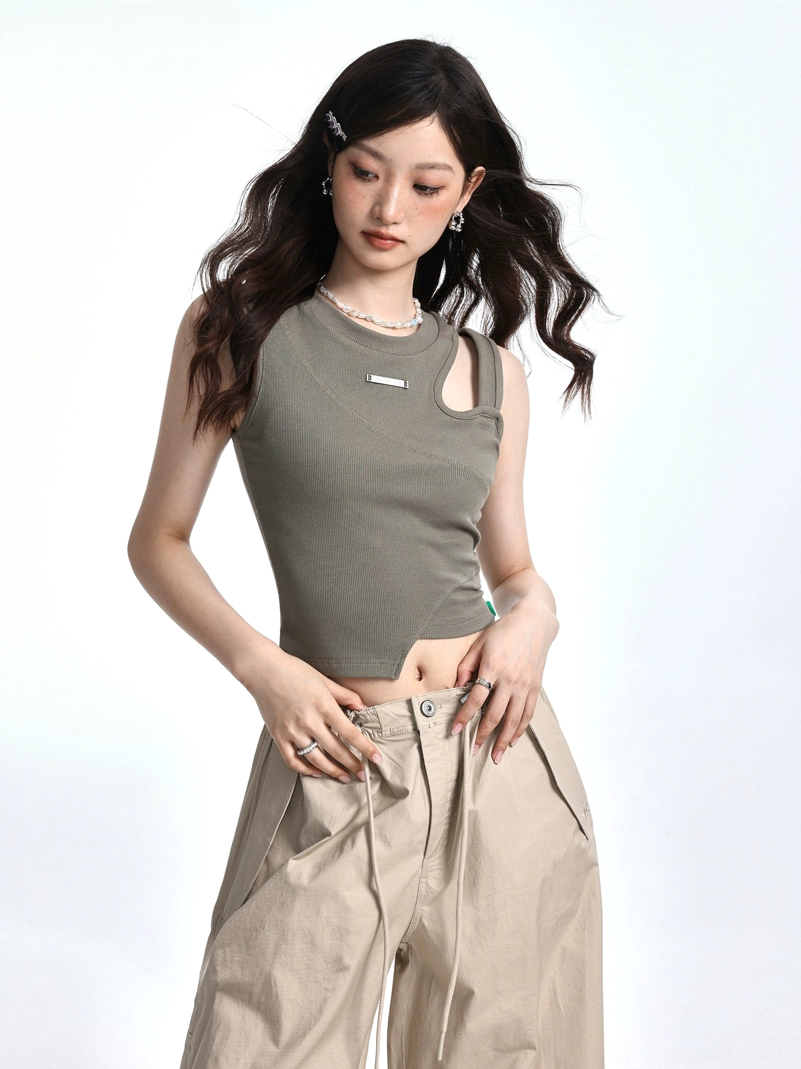 Close-up of Bean Paste Green ribbed asymmetric crop top with one shoulder cutout irregular curved hem and metal chest badge