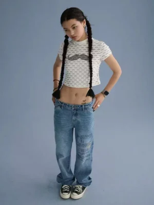 Beard and mustache graphic cropped streetwear tee styled with loose blue jeans and skate shoes in a full-body front view