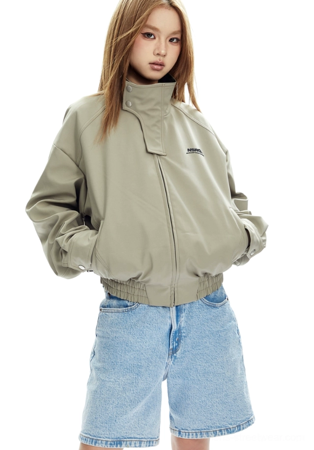 Front view of a beige boxy cropped bomber jacket with high stand collar, ribbed hem and cuffs, and light-wash jeans