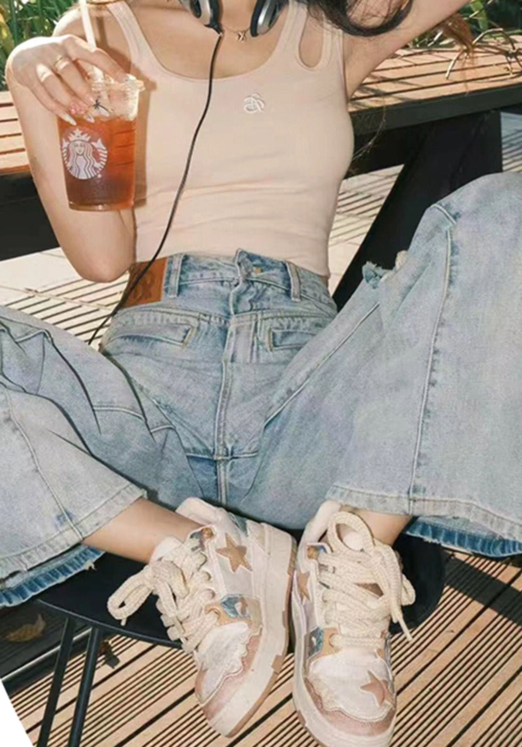 Overhead view of beige and brown jacquard star sneakers worn with wide-leg denim jeans at an outdoor cafe