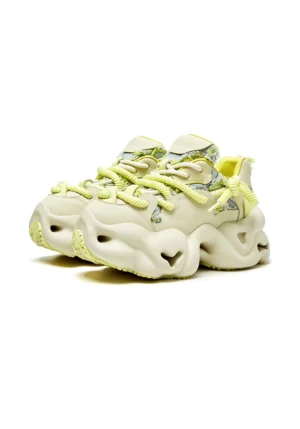 Beige chunky dad sneakers with neon yellow laces, layered leather-look panels, and an irregular platform outsole shown in a front three-quarter view