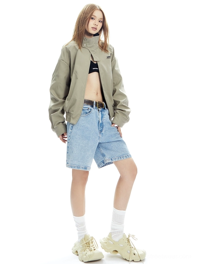 Full-body beige cropped bomber jacket outfit with high collar, dropped shoulders, ribbed trim, denim shorts, socks, and chunky sneakers