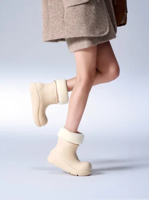 Woman wearing beige faux fur lined platform winter boots with a neutral wool coat and mini skirt in studio
