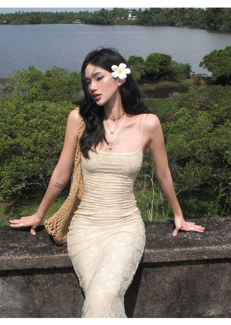 Beige floral lace mermaid maxi dress with fitted silhouette shown in a seated side view styled with a woven crossbody bag