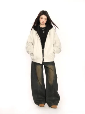 Full-body view of a beige layered hooded bomber jacket with black built-in hood, cropped bomber hem, relaxed fit, wide-leg washed jeans, and loafers