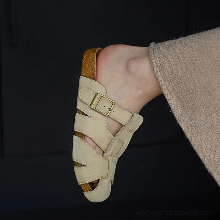 Beige leather fisherman sandals worn with relaxed trousers, featuring a closed cutout toe, adjustable side buckle, cushioned footbed, and cork-style midsole
