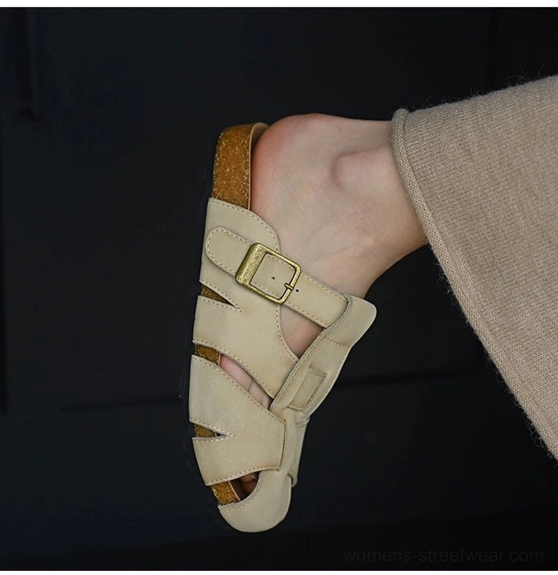 Back angled view of beige leather fisherman sandals worn with trousers, showing the adjustable side buckle, cutout upper, cork-style sole edge, and rubber outsole