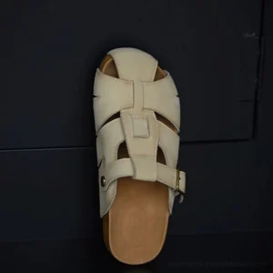 Beige leather fisherman sandals with woven cutout upper, rounded closed toe, adjustable gold-tone buckle strap, and layered cork-style sole shown from a top-down view