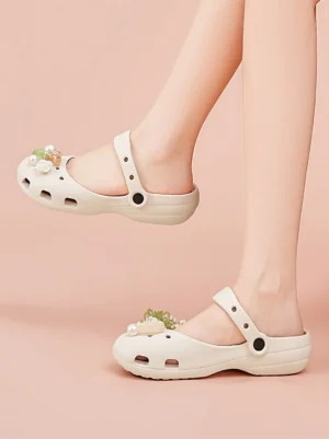 Off-white beige decorative Mary Jane slide sandals worn on feet against a light pink studio background with breathable hollow upper