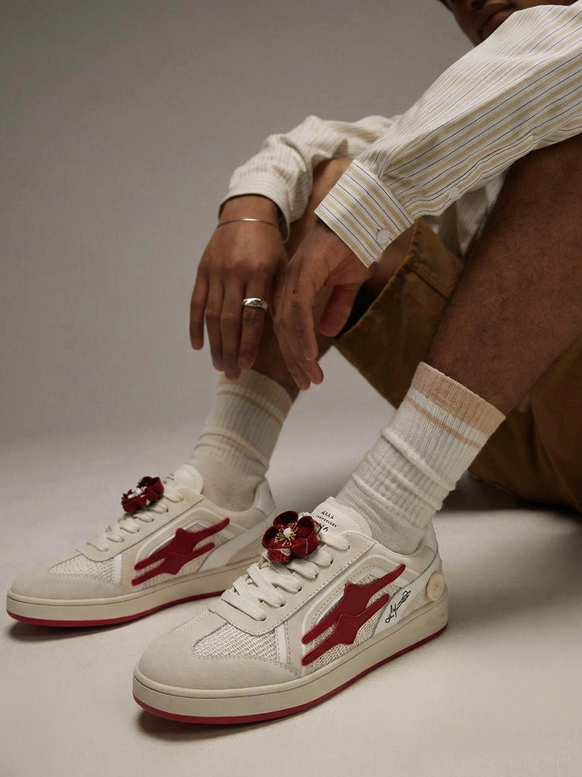 Beige and red retro casual training sneakers worn with a striped long-sleeve shirt, khaki shorts, and crew socks
