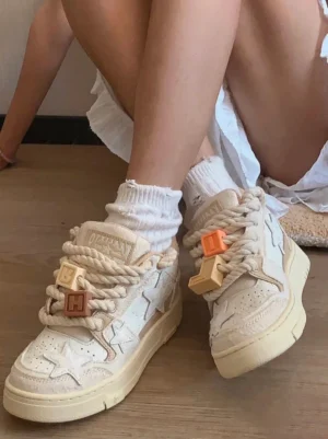 Beige star streetwear sneakers worn with white socks and a white dress, showing matching decorative lace charms and textured neutral upper