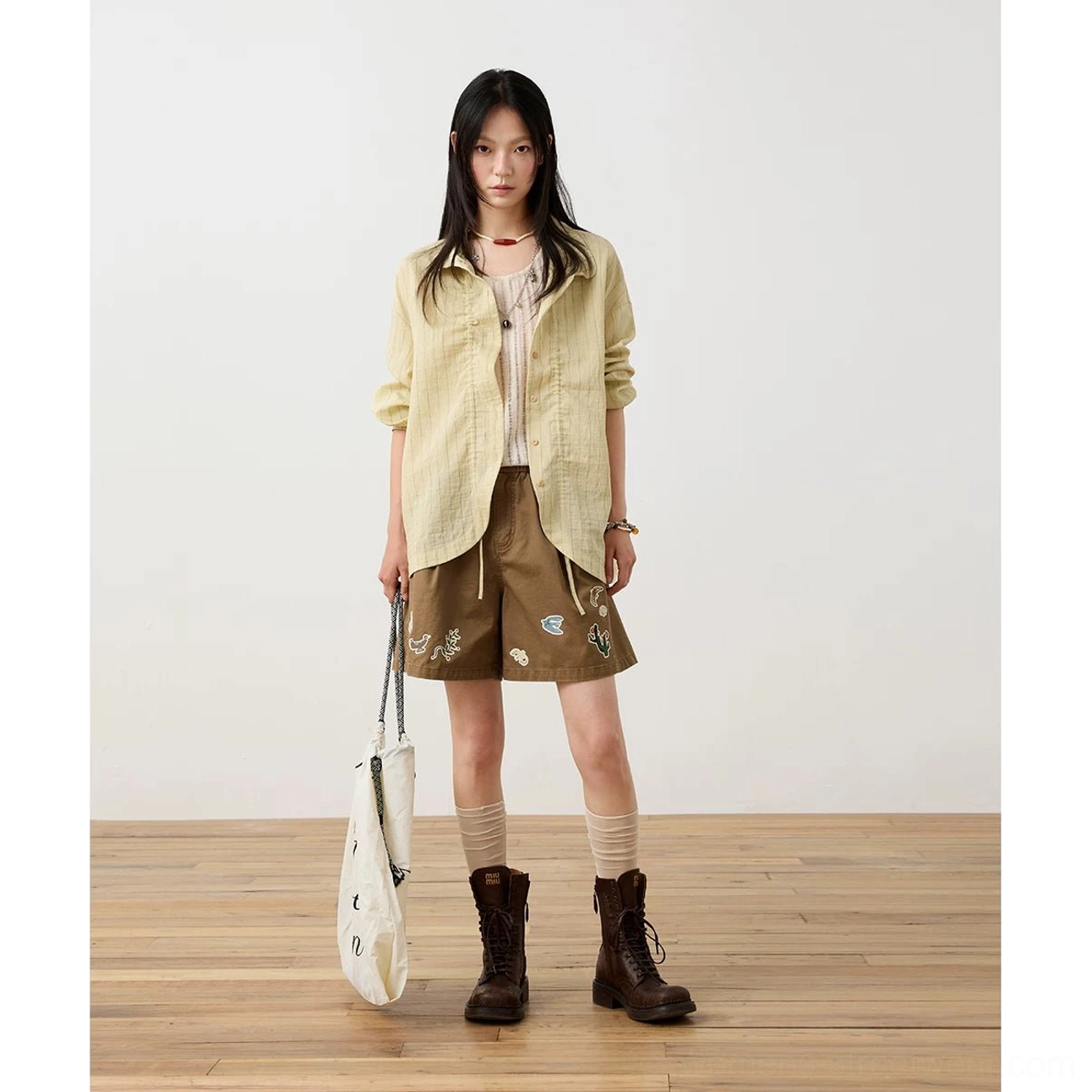 Beige textured striped Mandarin collar shirt styled with a camisole, embroidered brown shorts, brown socks, combat boots, and printed canvas tote