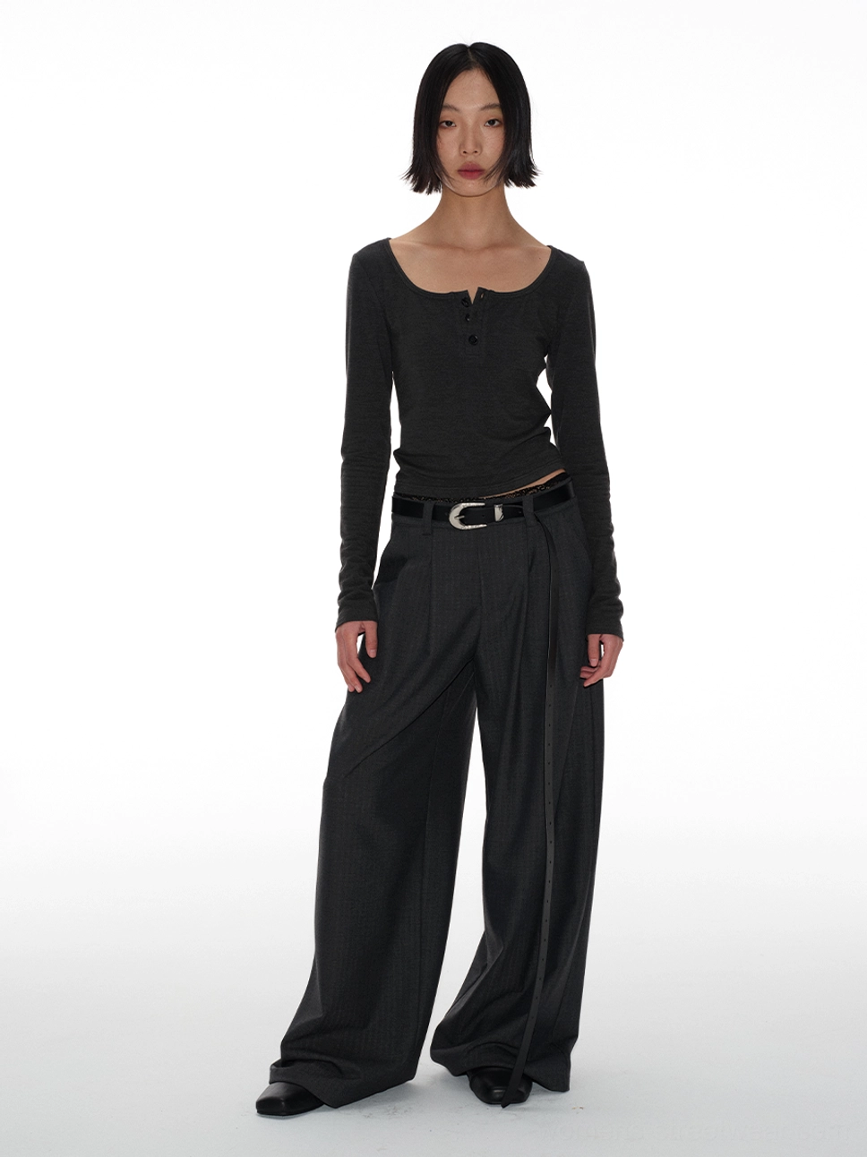 Full-body front view of charcoal gray belted wide-leg tailored streetwear trousers with a high waist, double pleats, and long draped legs