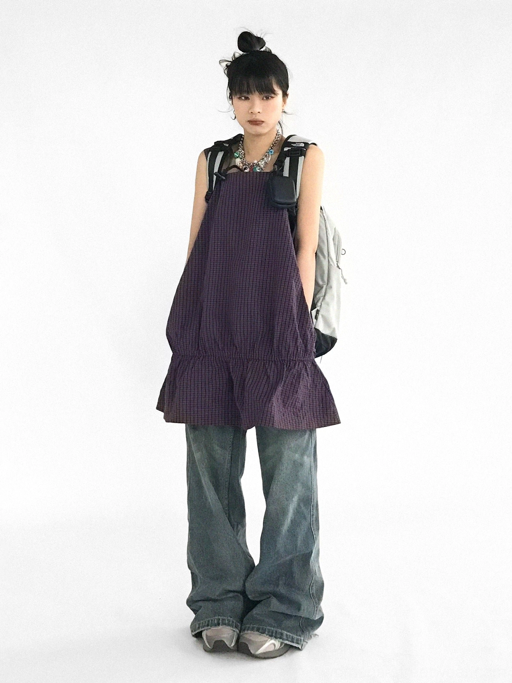 Berry plaid ruffled pinafore mini dress layered over wide leg jeans with backpack and necklaces