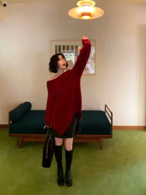 Berry red oversized off-shoulder knit sweater with asymmetric hem and long sleeves styled with knee-high boots and handbag
