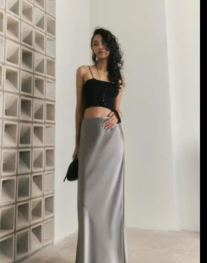 Agate grey satin bias-cut fishtail maxi skirt styled with a black cropped camisole in a minimalist studio front view