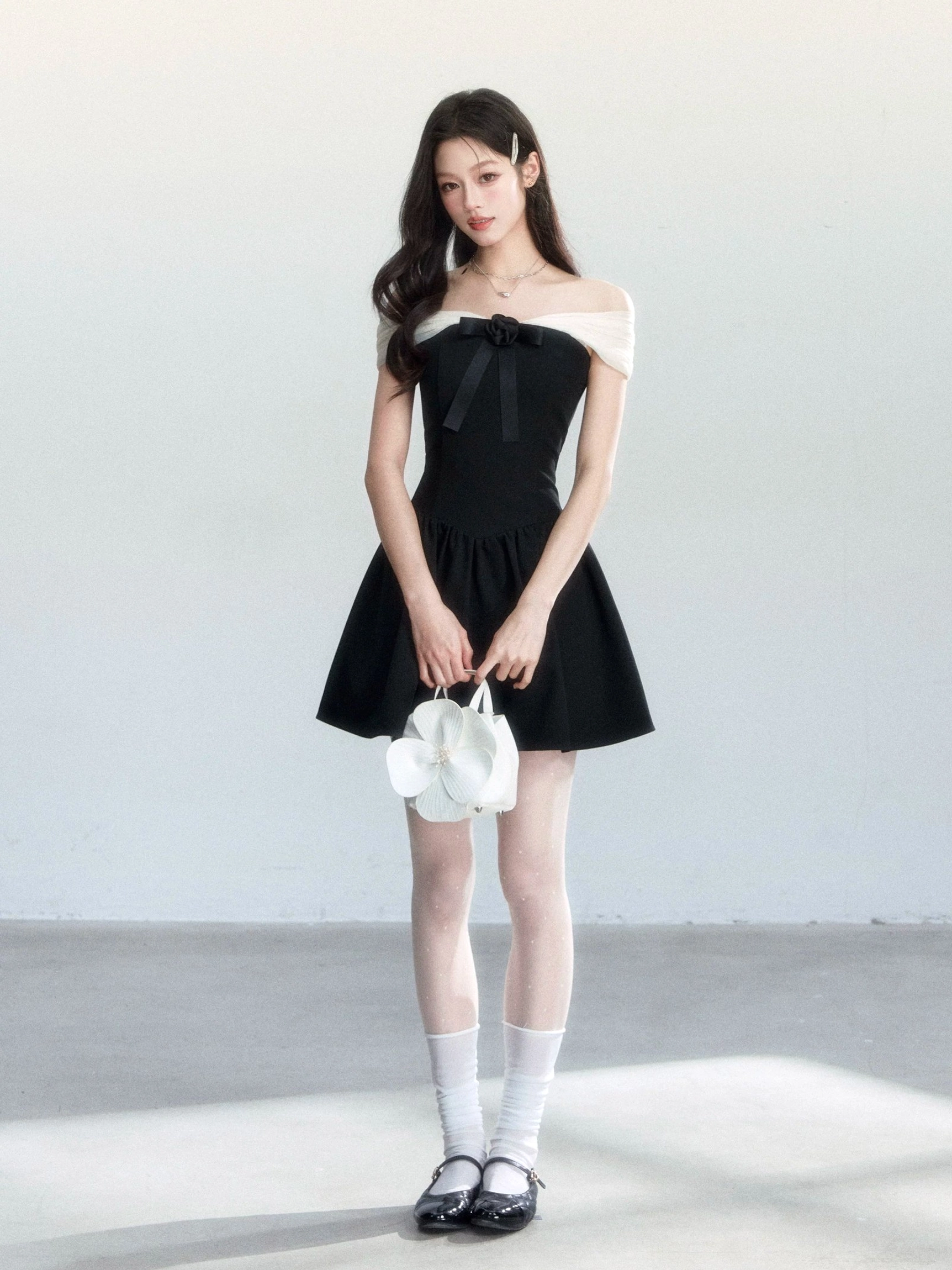 Full-body black A-line bow mini dress with light mesh shoulder detail styled with white socks and leather Mary Jane shoes