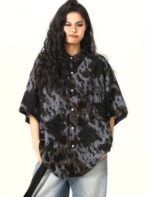 Front view of black abstract tie-dye oversized short-sleeve button-up shirt styled with light wash wide-leg jeans