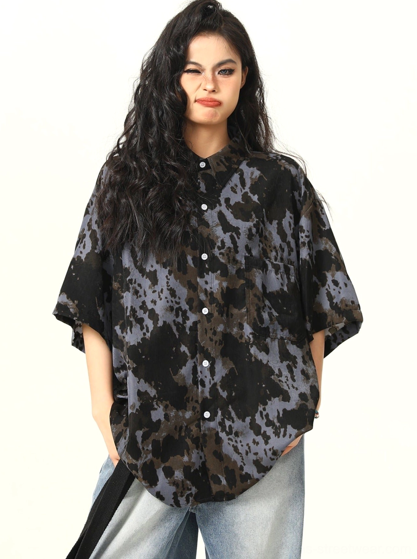 Front view of black abstract tie-dye oversized short-sleeve button-up shirt styled with light wash wide-leg jeans