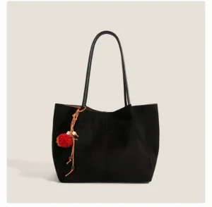Black faux suede Korean streetwear tote bag with smooth shoulder straps and red pom pom tassel charm on a light beige background