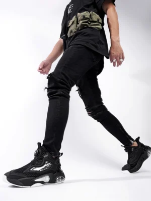 Black air cushion streetwear runner sneakers shown on foot with ripped black jeans and a waist bag