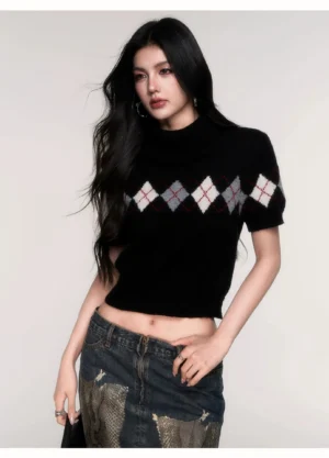 Front view of a black cropped argyle knit sweater with soft turtleneck collar, short puff sleeves, fitted waist-level silhouette, and classic contrast diamond pattern