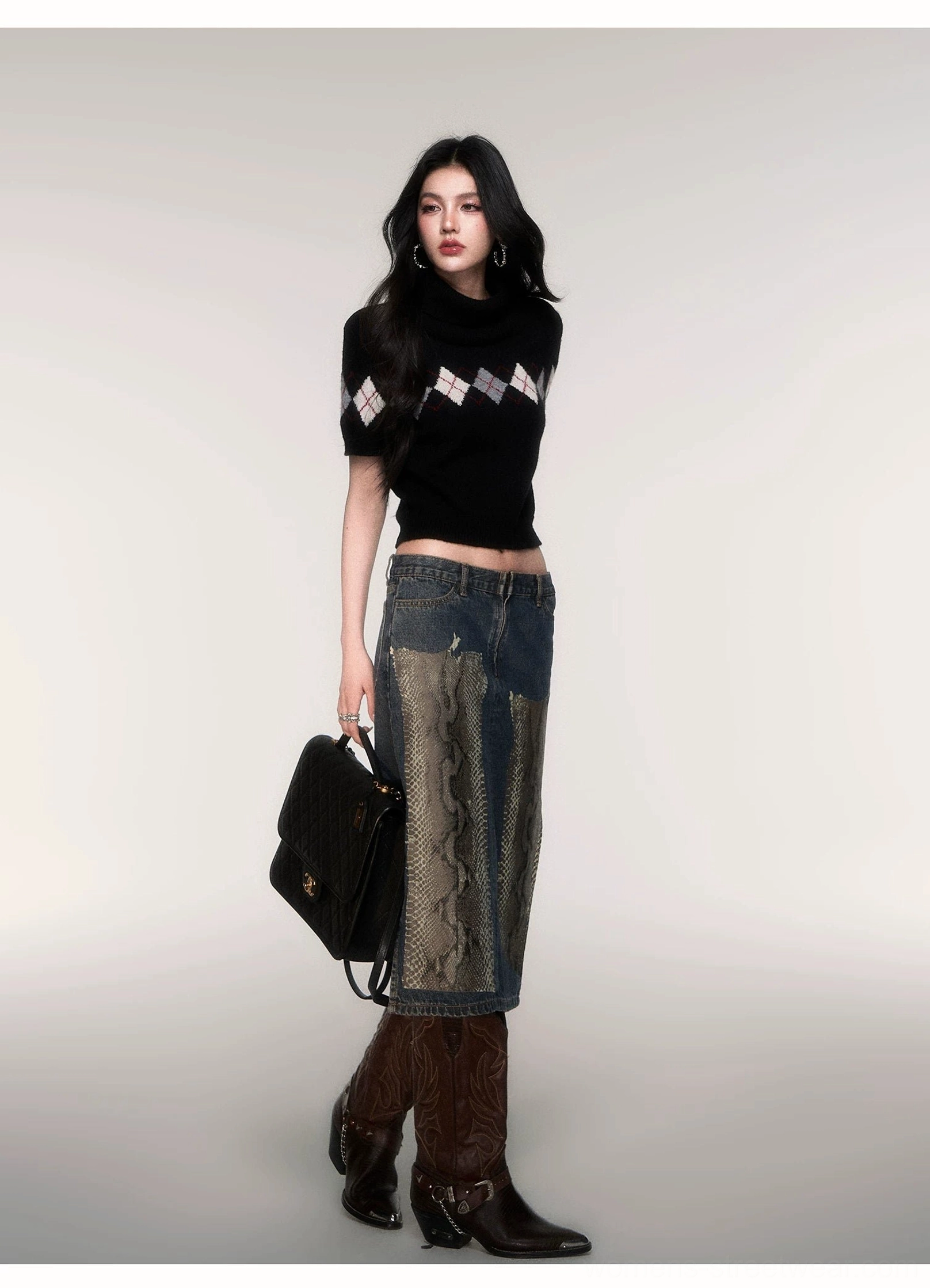 Side view of a black argyle cropped knit turtleneck sweater styled with a denim midi skirt, cowboy boots, and black leather handbag