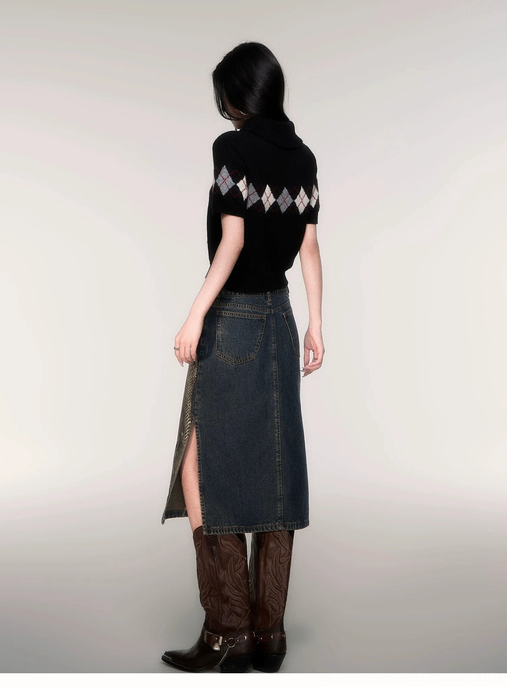 Back view of a black cropped argyle turtleneck sweater showing the upper-back diamond pattern, short sleeves, and waist-level hem with split denim skirt