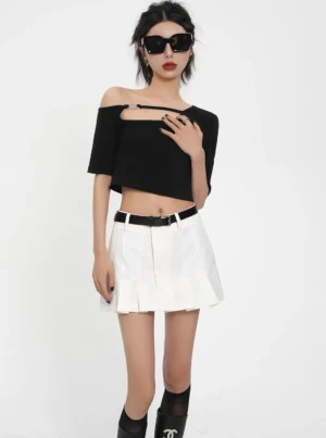 Black asymmetric off-shoulder buckle cut-out ribbed crop top styled with white pleated mini skirt and boots
