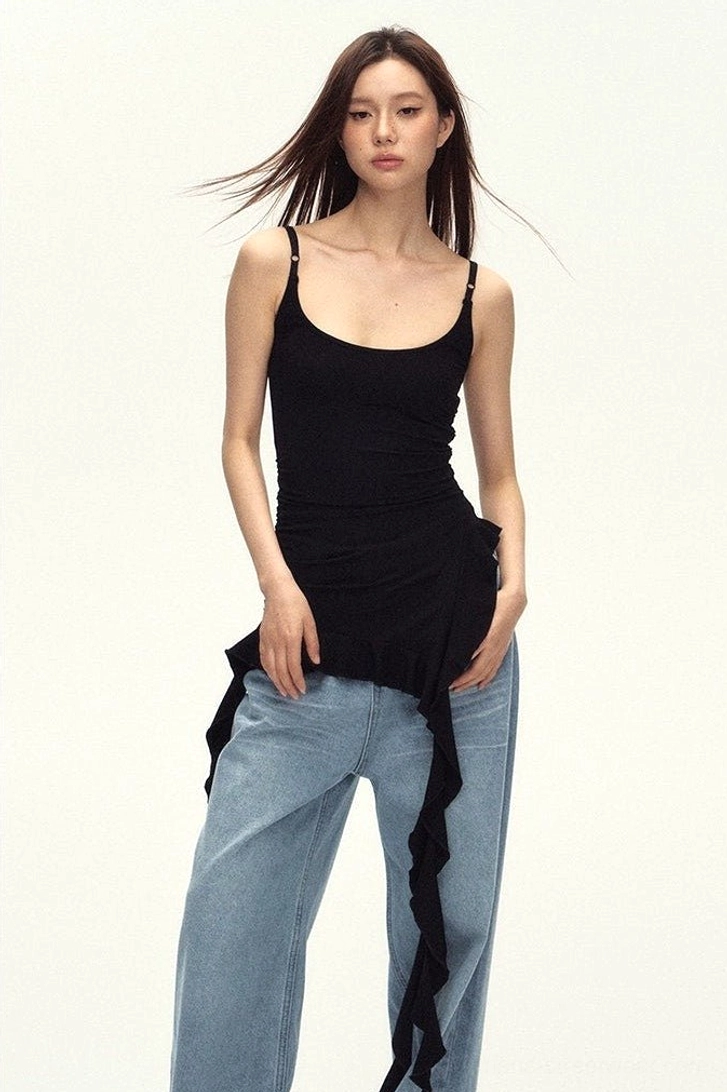Model wearing a fitted black asymmetric cami top with scoop neckline and trailing ruffled hem in a modern streetwear outfit