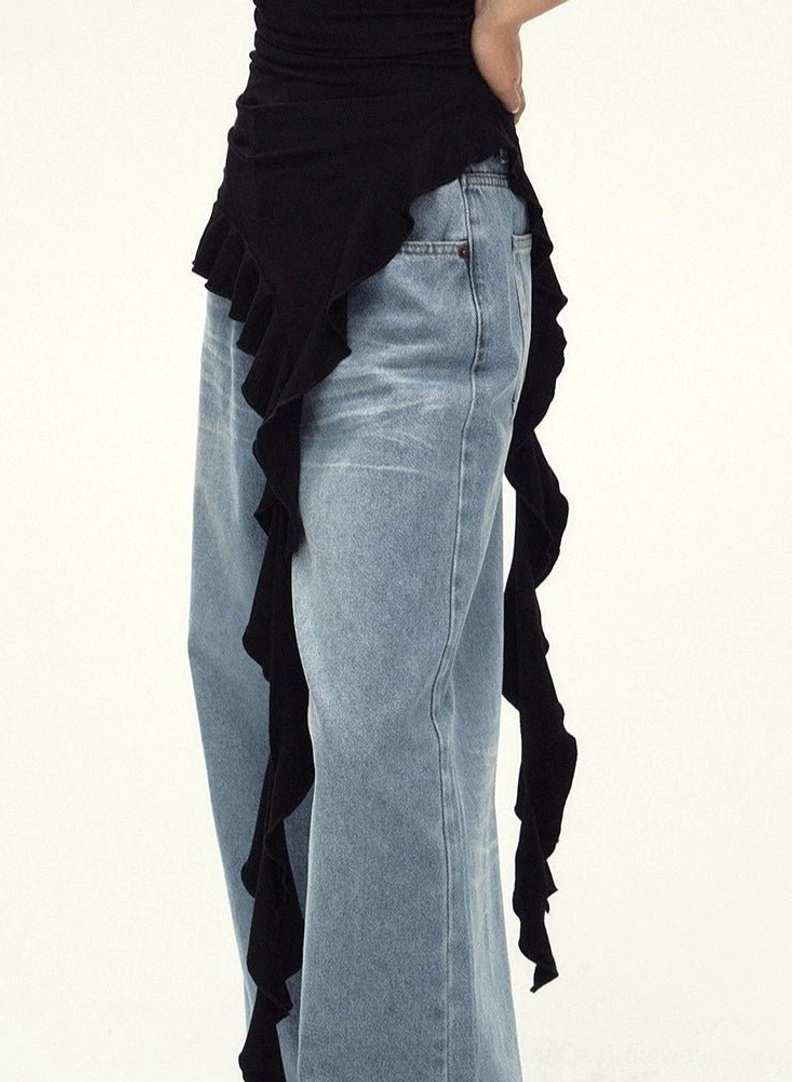 Detail view of the flowing asymmetric ruffled hem on a black streetwear cami top worn with loose light-wash denim