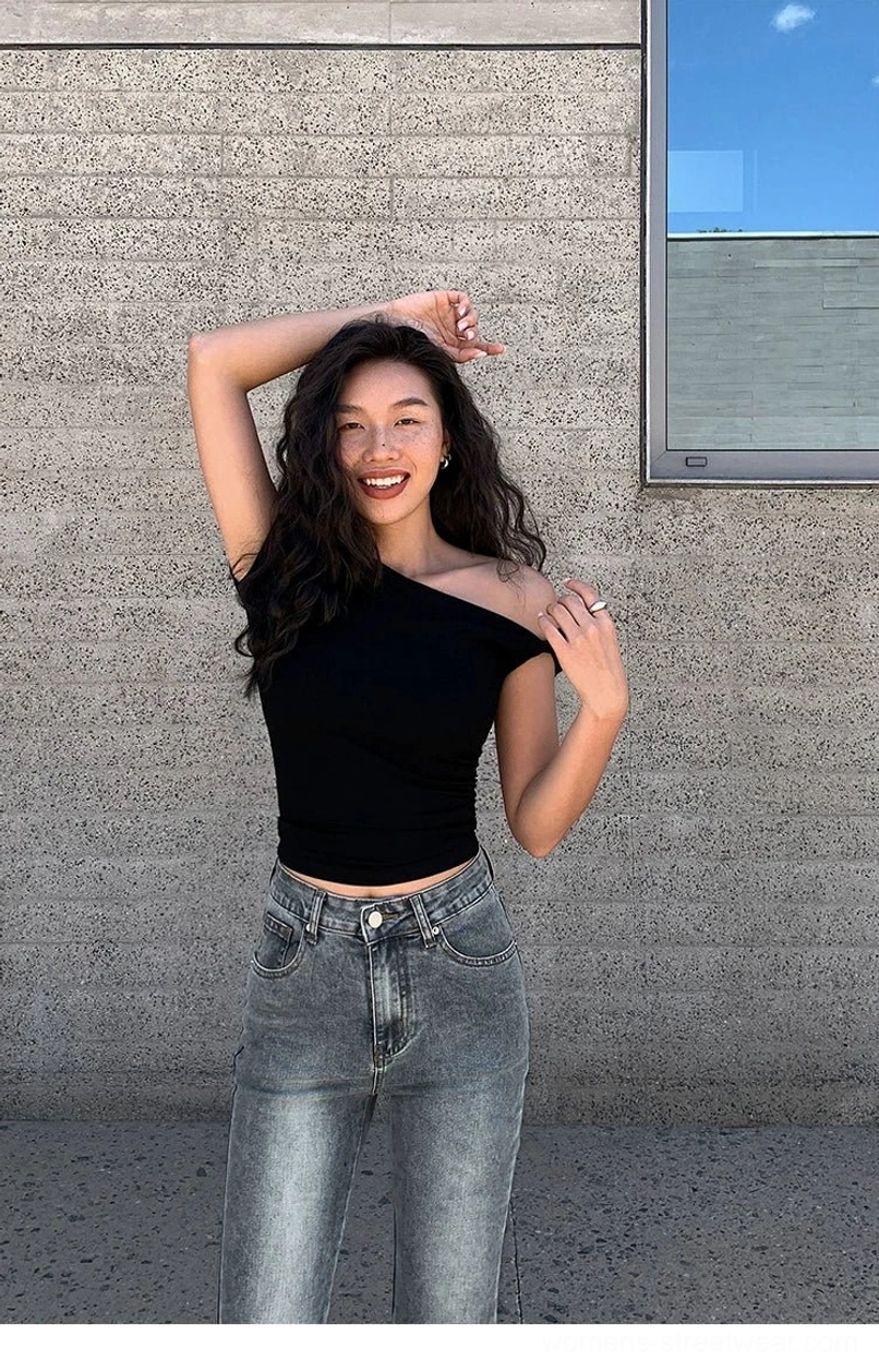 Black fitted asymmetric crop tee with one short sleeve and a bare shoulder styled with high-rise blue denim
