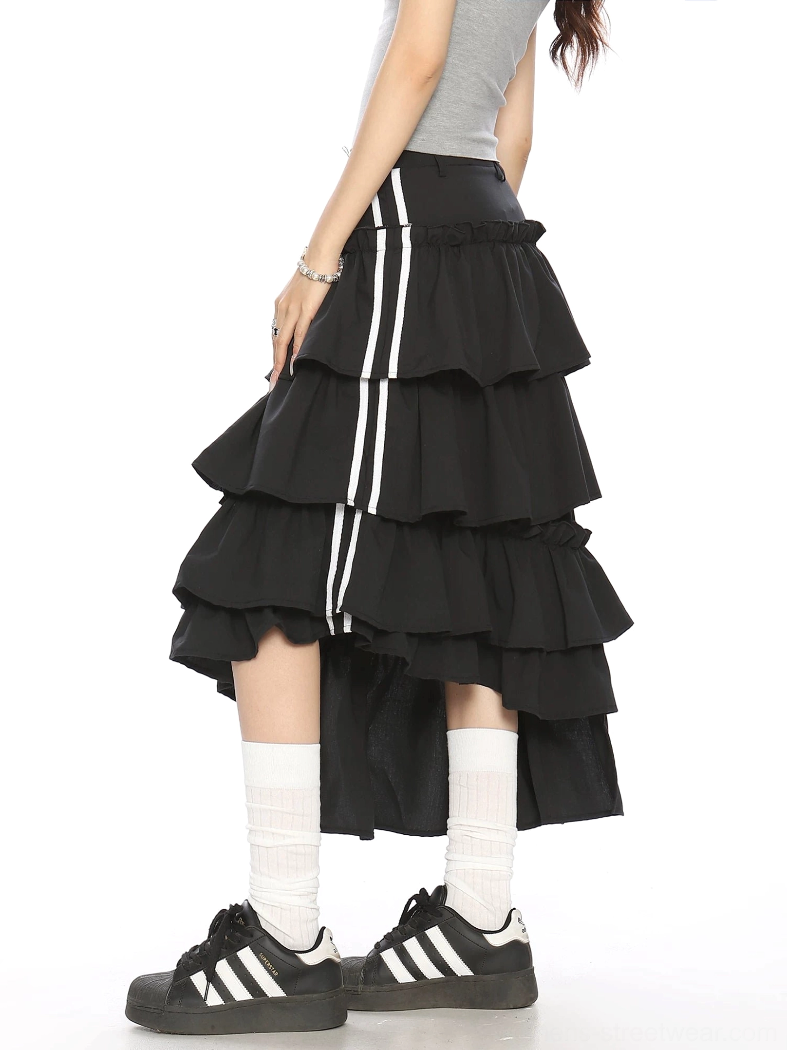 Side back view of black asymmetric midi skirt with layered ruffles dual white stripe ribbon accents and irregular hemline