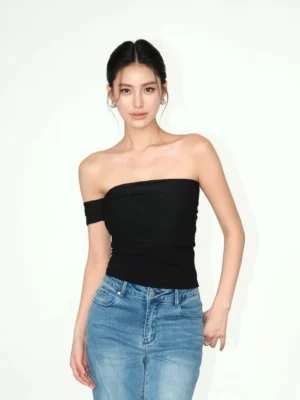 Black asymmetric off-shoulder ruched crop top styled with blue straight-leg jeans in a minimalist studio