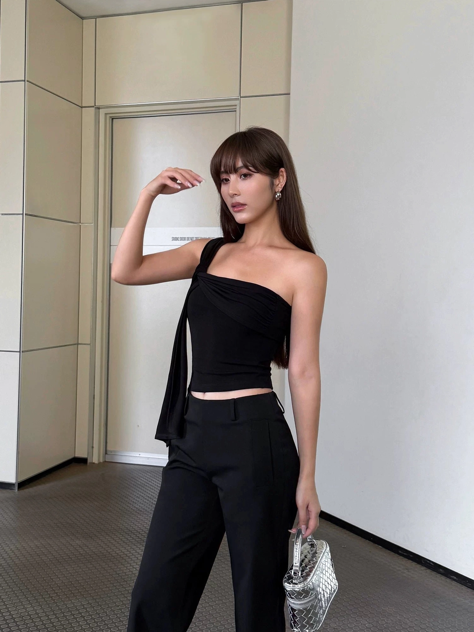 Black asymmetric one-shoulder cropped top with hanging shoulder sash styled with high-waisted black trousers