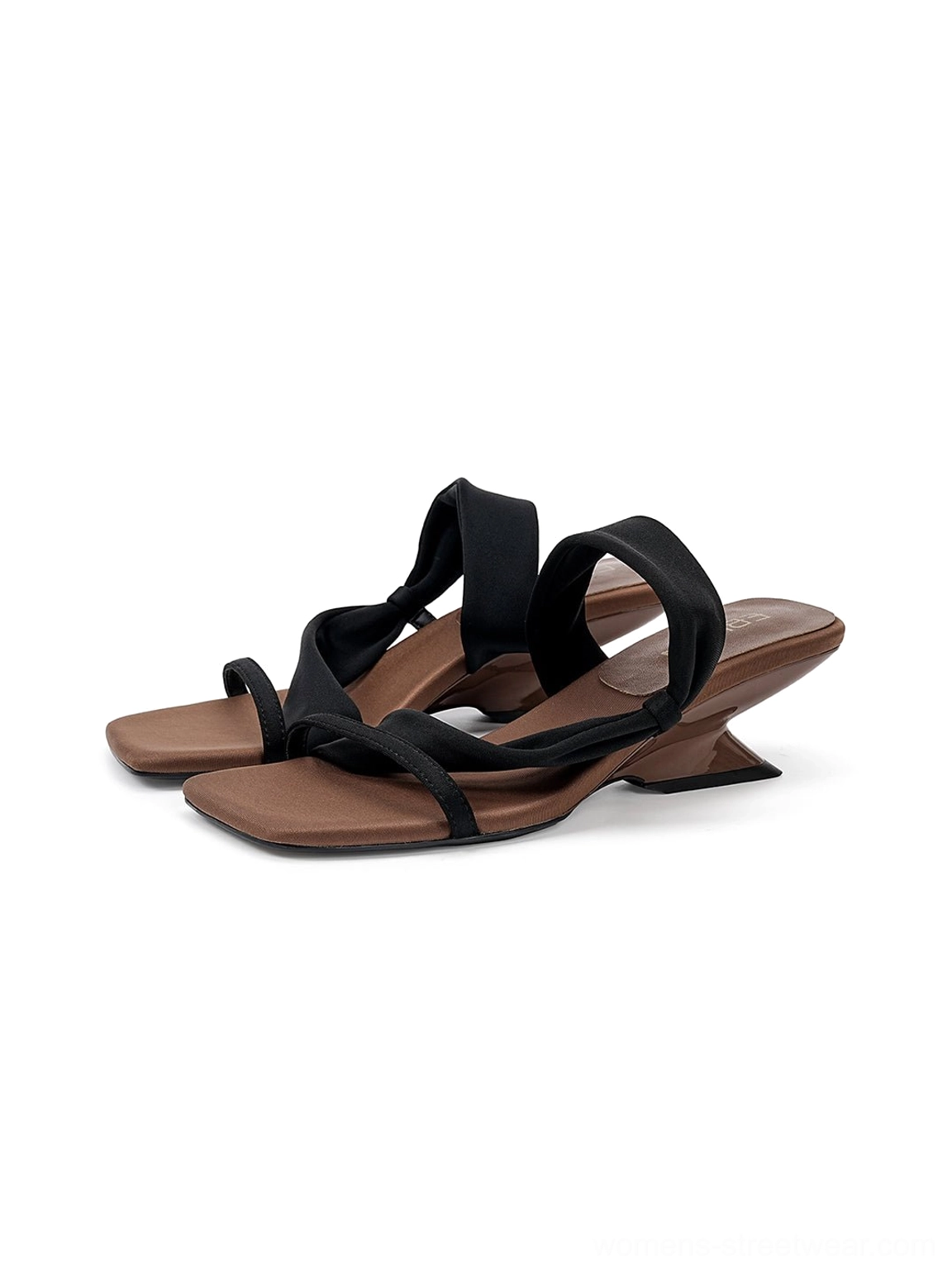 Rear three quarter view of black asymmetric strap sandals with exposed curved wedge heels and brown footbeds