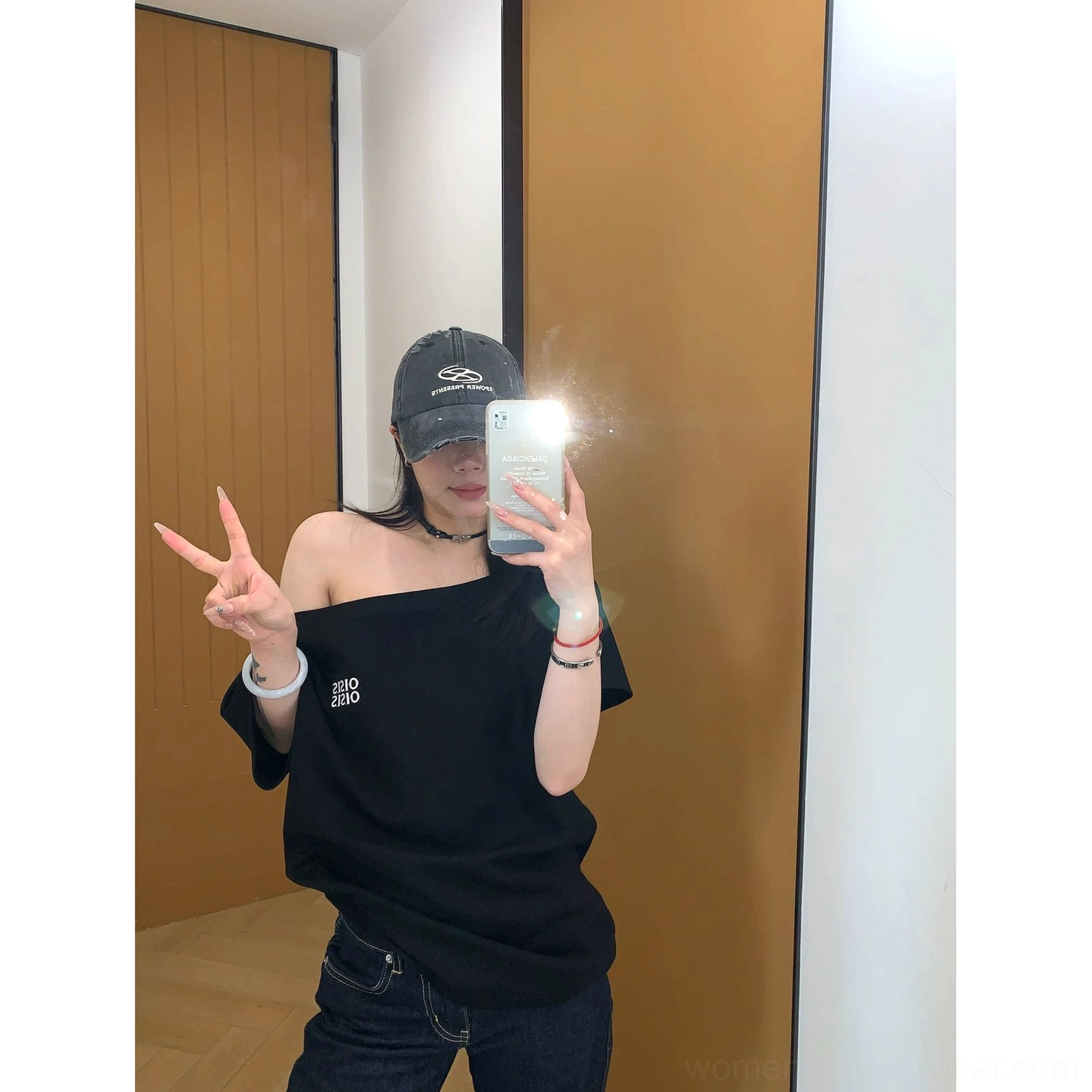 Front mirror outfit view of a black asymmetrical off-shoulder streetwear tee styled with dark jeans and delicate bracelets