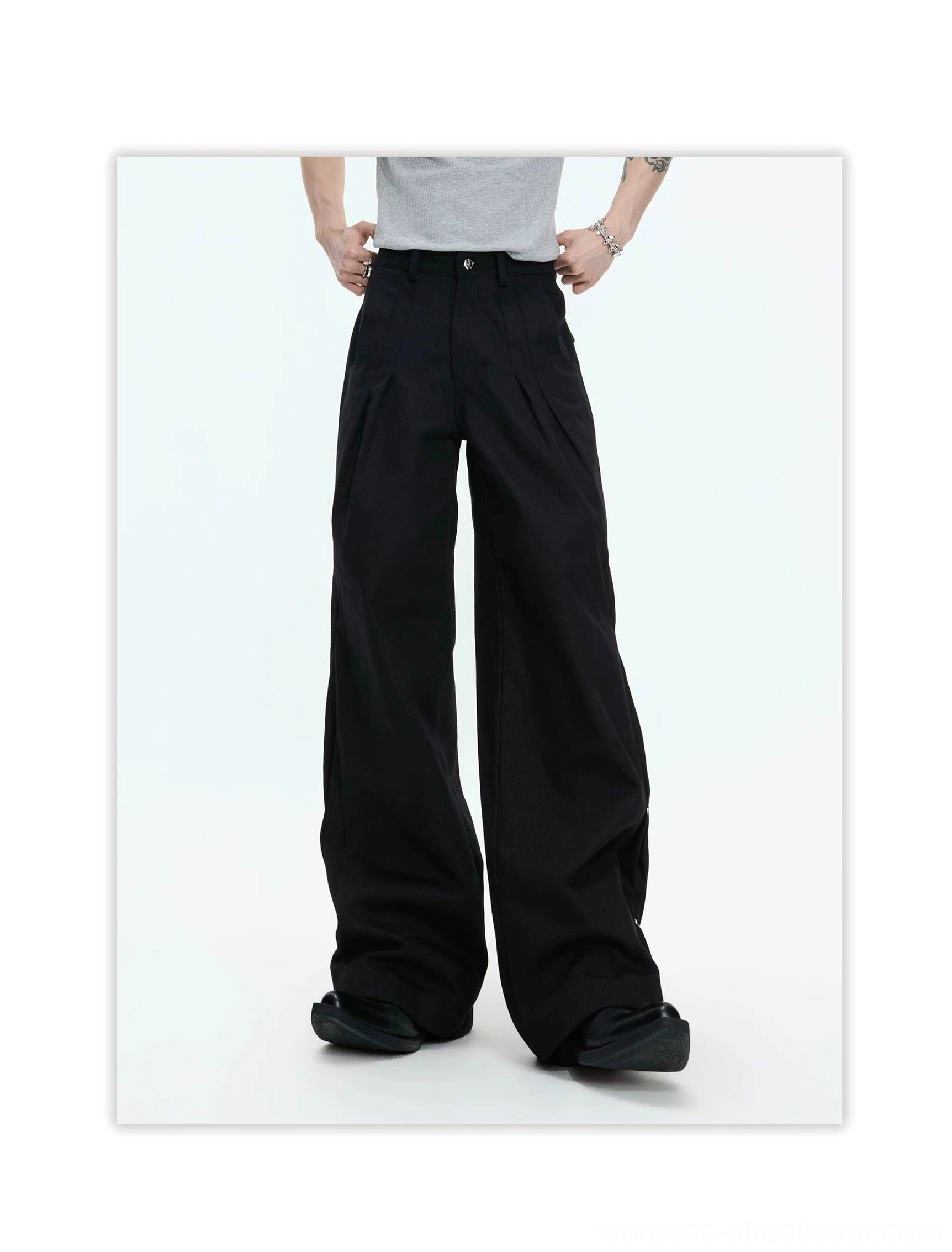 Black avant-garde wide-leg streetwear pants shown from the front with a high-waisted fit, structured front pleats, matte cotton fabric, and oversized draped legs