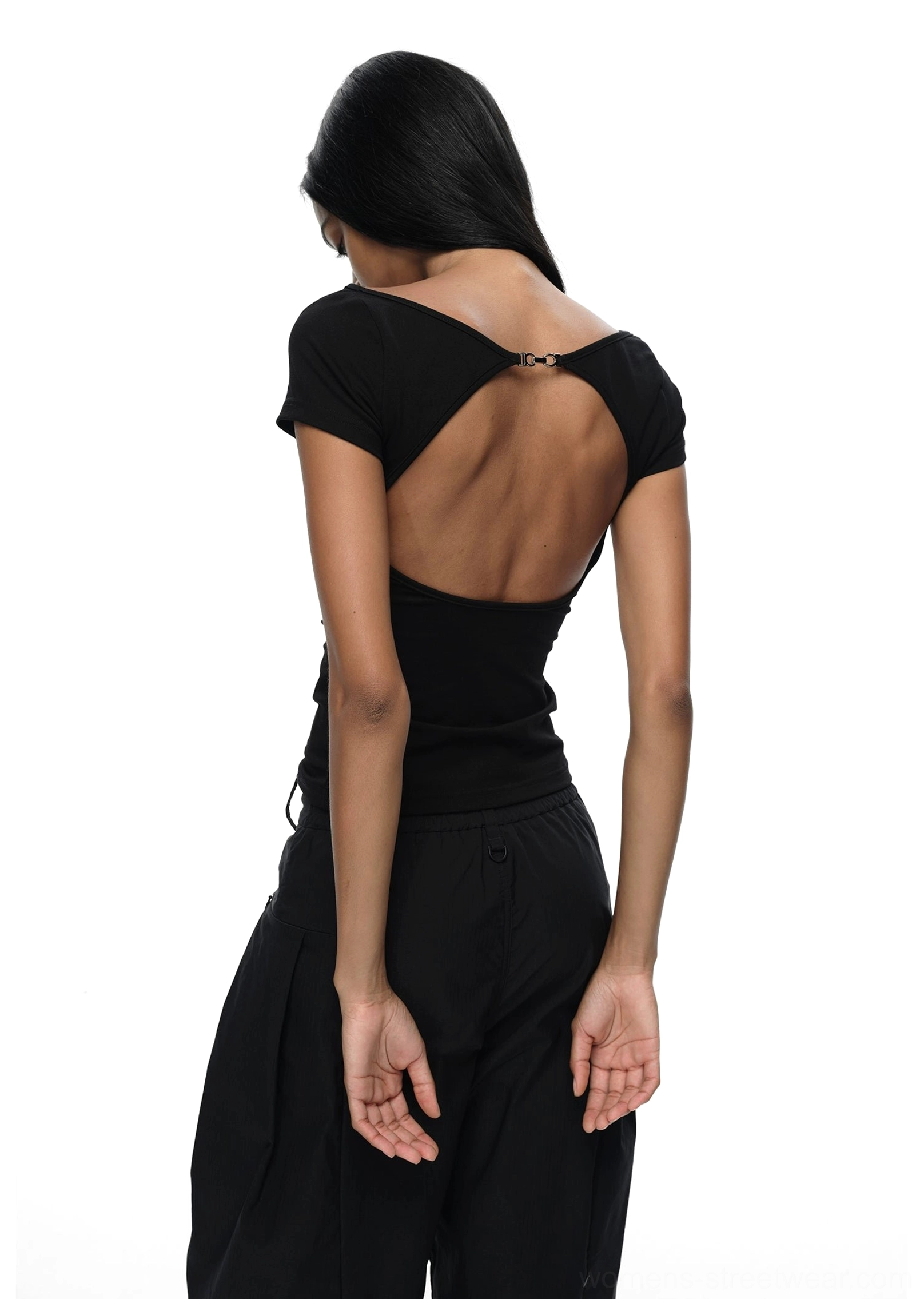 Black backless fitted streetwear T-shirt with metallic upper-back buckle detail styled with black wide-leg trousers