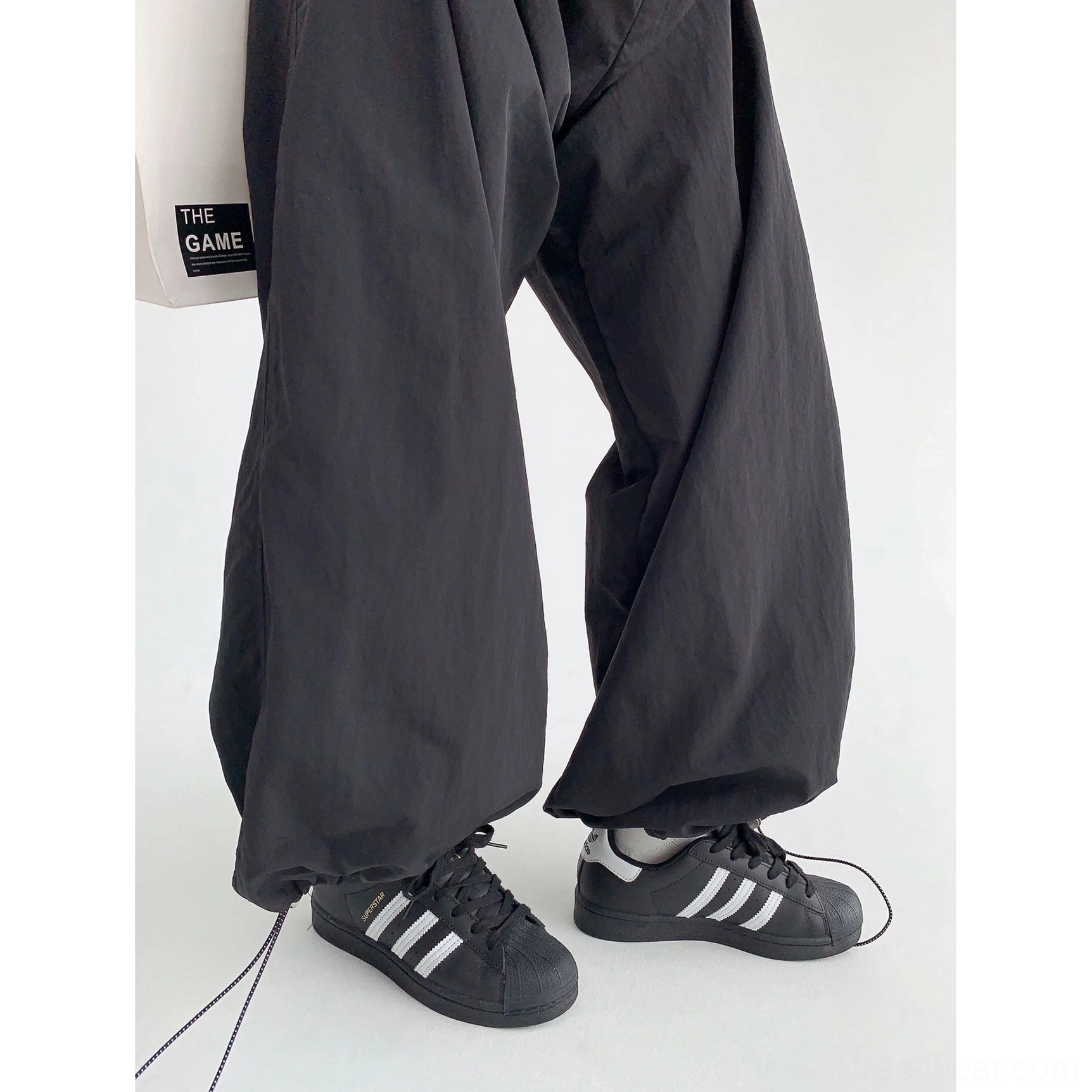 Black baggy parachute streetwear pants with adjustable drawstring cuffs and oversized legs styled with classic sneakers